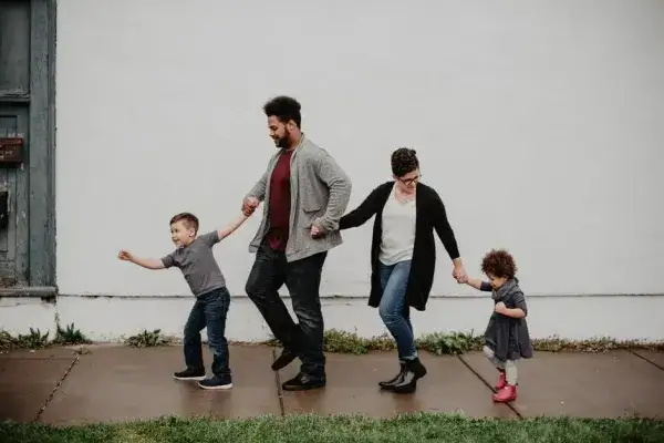 Two foster parents and two young children holding hands and walking down the street