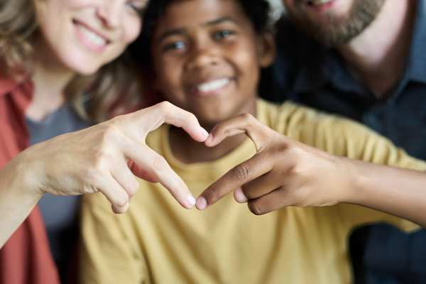 A adoptive family with a child making a heart with his hands