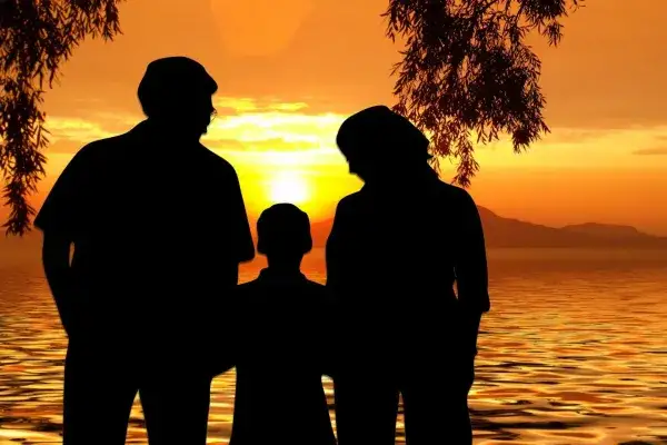 Silhouette of man and women on either side of young child looking at the sunset