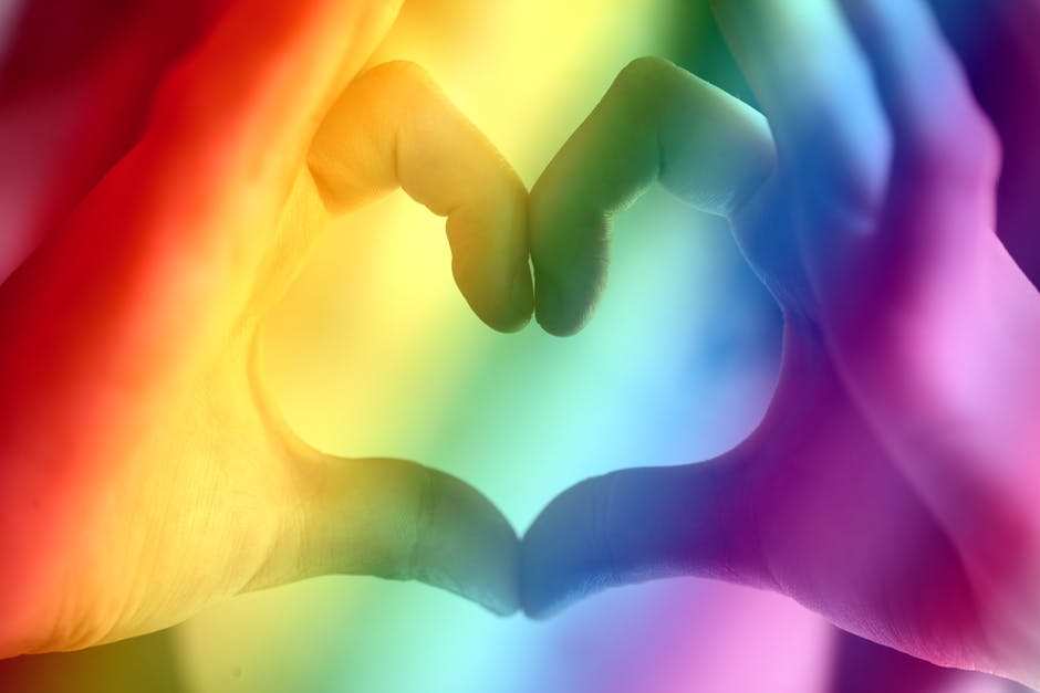 LGBTQ Love heart made from hands with a rainbow behind it