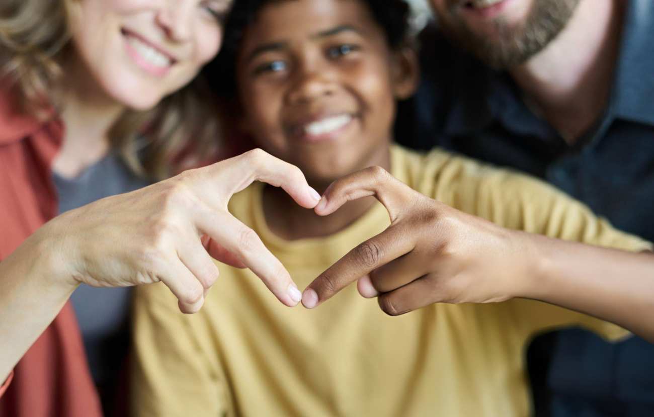 A adoptive family with a child making a heart with his hands