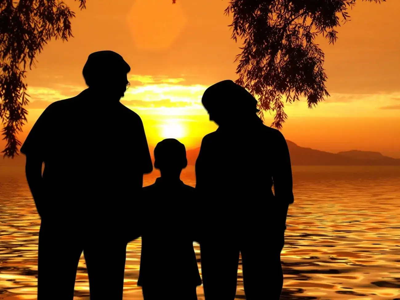 Silhouette of man and women on either side of young child looking at the sunset
